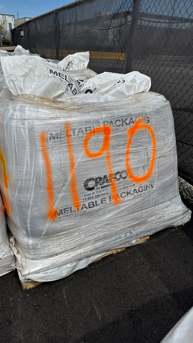 A large white plastic meltable packaging bag with orange spray-painted numbers '1190' on the front, photographed outdoors on a dark surface with a chain-link fence in the background.